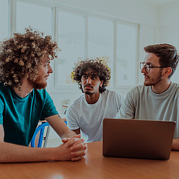 eine Gruppe von Studierenden sitzt in einem Seminarraum und diskutiert mit Laptop 