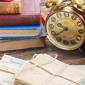 Nahaufnahme einer antiken Uhr auf einem Schreibtisch mit alten Briefen und Büchern. 