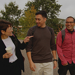 zeigt drei junge Studierende der Europa-Universität Flensburg draußen auf dem Campus während eines Gesprächs