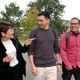 zeigt drei junge Studierende der Europa-Universität Flensburg draußen auf dem Campus während eines Gesprächs