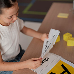 ein Kind bei der Sprachtherapie hält verschiedene Wortkarten sitzend am Tisch. 