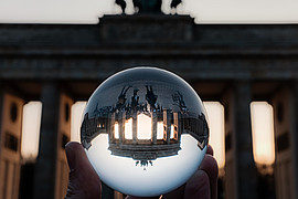 Das Brandenburger Tor spiegelt sich in einer Glaskugel, die von einer Hand gehalten wird.