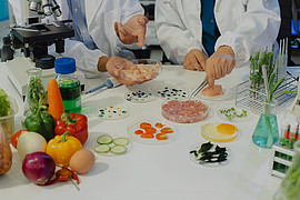 zwei Menschen führen Experimente mit Lebensmitteln durch. Auf einem Tisch stehen unterschiedliche Gemüsesorten 