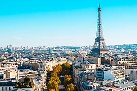 zeigt eine Luftaufnahme mit Eiffenturm von Paris unter blauem Himmel