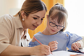 Eine Frau und ein Mädchen sitzen an einem Tisch und malen gemeinsam mit Buntstiften auf Papier.