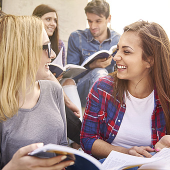Gruppe von Jugendlichen sitzt draußen auf Stufen und liest gemeinsam in Büchern.