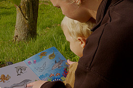 zeigt eine Studierende der Uni Flensburg vorlesend aus einem Tierbuch und einem Kind