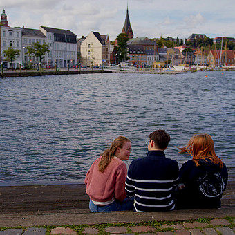 eine Gruppe drei Studierender sitzt am Flensburger Hafen 