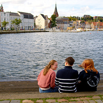 eine Gruppe drei Studierender sitzt am Flensburger Hafen 
