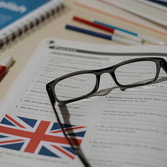 Eine Brille liegt auf einem Englisch Buch. Die Aufgabenstellungen sind leicht verschwommen. Die Brittische Fahne ist unten links auf dem Englisch Buch zu erkennen. 