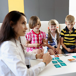 drei Kinder sitzen vor einem weißen Tisch mit Lernkarten 
