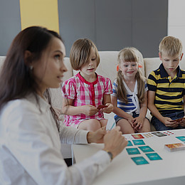 drei Kinder sitzen vor einem weißen Tisch mit Lernkarten 