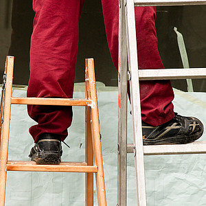 Bild eines Mannes, der auf zwei unterschiedlich großen Leitern steht