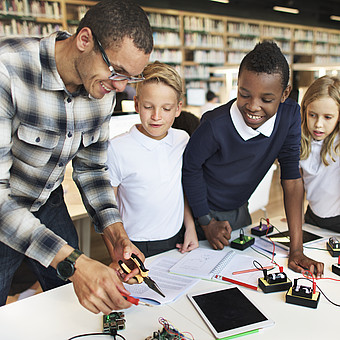 Eine Lehrperson macht eine Unterrichtseinheit zur Elektrotechnik mit drei Kindern 