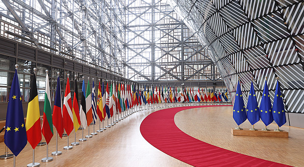 Blick ins moderne Foyer des Europa-Gebäudes mit einem roten Pfad und den aufgereihten europäischen Flaggen.