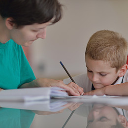 Kind sitzt mit Block und Lehrkradt an einem Tisch und köst konzentriert Aufgaben 