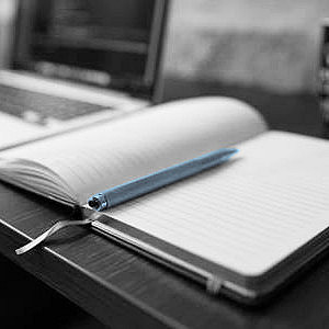 Bild eines Schreibtisches mit Laptop und aufgeschlagenem Buch