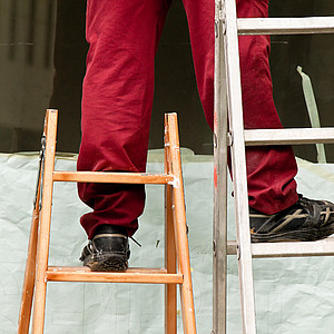 Bild eines Mannes, der auf zwei unterschiedlich großen Leitern steht