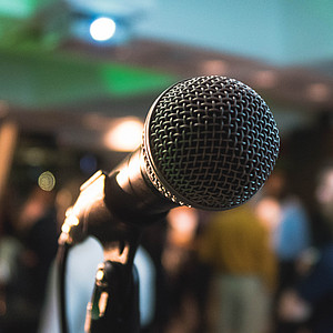 Bild eines Mikrofons vor unscharf gestelltem Hintergrund einer Veranstaltung