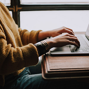 Eine Person sitzt an einem Tisch, auf dem ein Laptop liegt. Sie schreibt auf der Tatstatur.