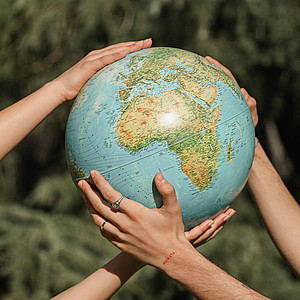 Das Bild zeigt zwei Paar Hände, die einen Globus halten.