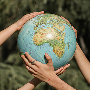 Das Bild zeigt zwei Paar Hände, die einen Globus halten.