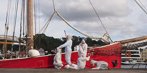 Fünf Studierende in einer darstellenden Pose vor einem alten roten Segelschiff