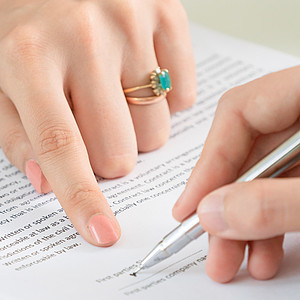 Eine Frauenhand deutet auf eine zu unterschreibende Stelle auf einem Vertrag