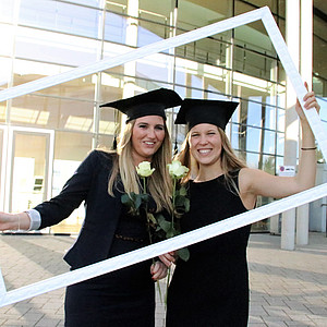 Zwei Absolventinnen des IIM-Studiengangs halten einen Bilderrahmen