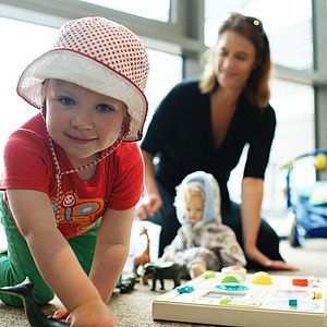 Foto eines spielenden Kindes mit Frau im Hintergrund