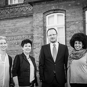Schwarz/ weiß Foto von drei Frauen und einem Mann vor Universitätsgebäude.
