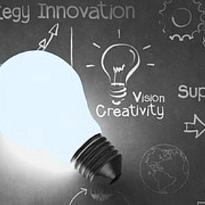 Eine Glühbirne liegt auf einer Tafel, auf der mit Kreide die Wörter Strategy Innovation, Vision Creativity, Solution und Support stehen.