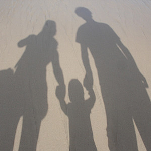 Das Foto zeigt einen Schatten von 2 erwachsenen Personen und 2 Kindern, die alle zusammen stehen und eine Familie sein können